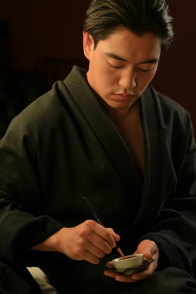 pexels-photo-7610579-7610579 Asian male artist concentrating on calligraphy indoors, holding a paintbrush.